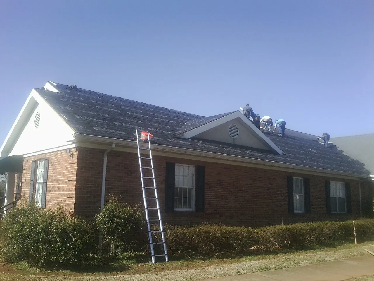 Crew tearing shingles off a brick ranch roof with a ladder set — Emergency Roof Repair work by our crew in Riceboro