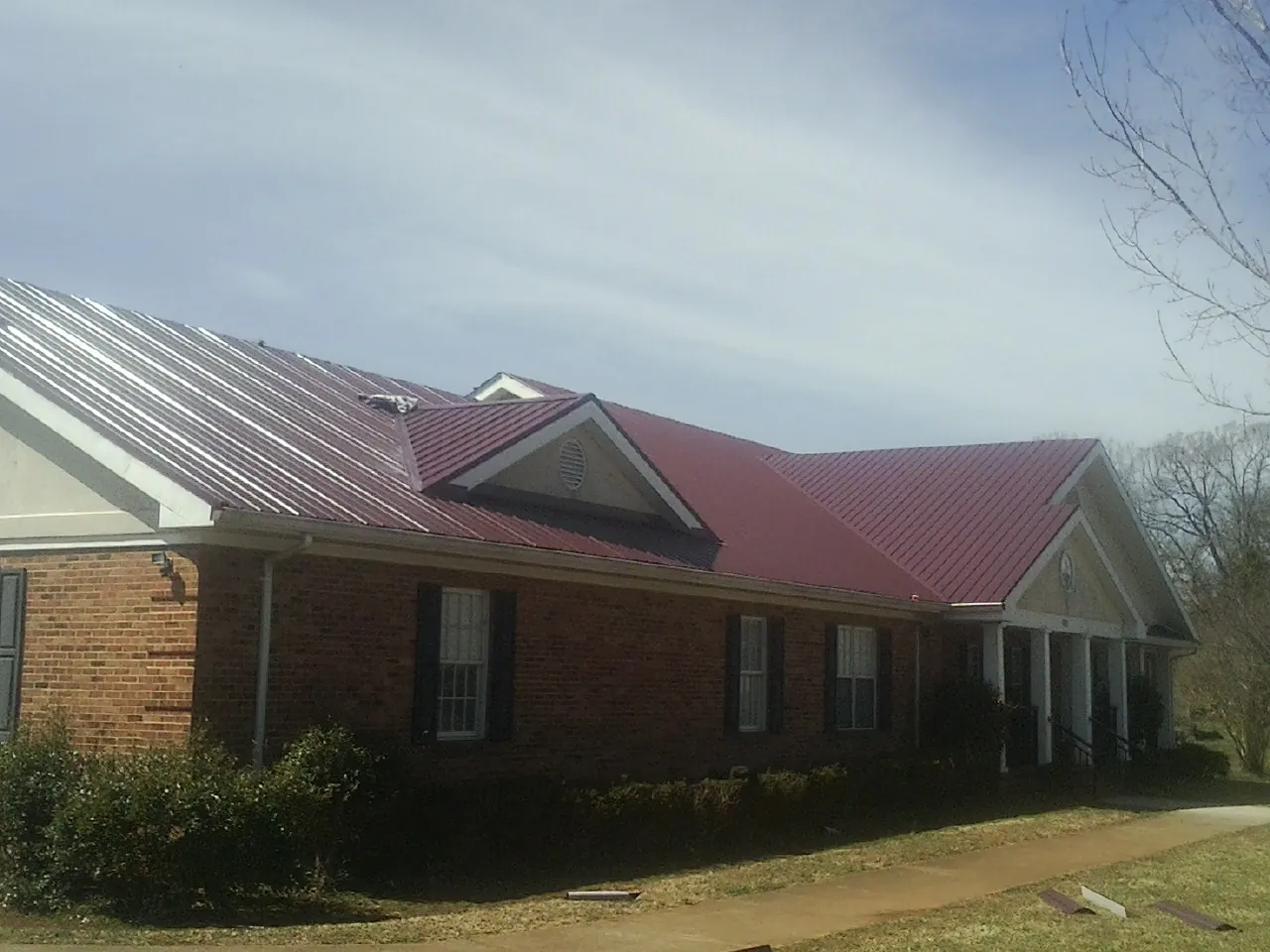 Red metal roof with gabled entries on a long brick building, from a Hail Damage Roof Repair job in Riceboro