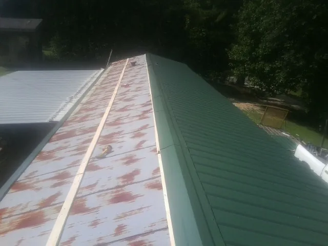 Old rusted panels beside newly installed green metal roofing — Wind Damage Roof Repair by Roofing Brothers in Riceboro