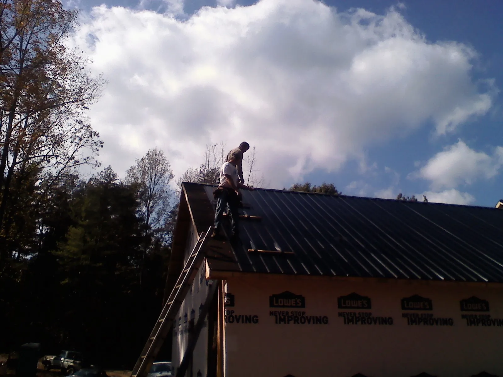Roofer fastening dark metal panels high against a cloudy sky, from a Roof Inspection job in Riceboro