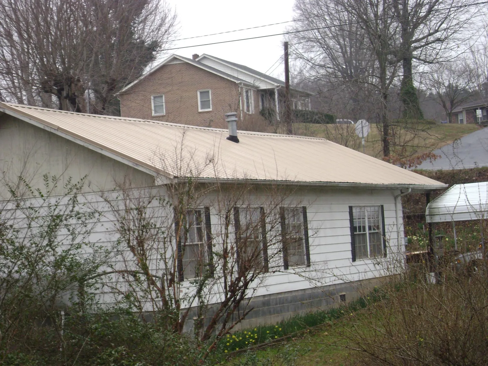 Tan metal roof on a white sided house set into a hillside — Commercial Roofing by Roofing Brothers in Riceboro